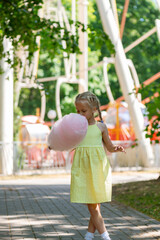 Blonde girl with pink cotton candy in the amusement park.