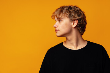 Young curly man looking to the side against yellow background - obrazy, fototapety, plakaty