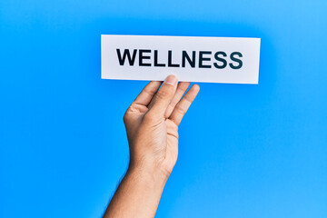Hand of caucasian man holding paper with wellness word over isolated blue background