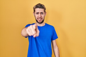 Hispanic man with beard standing over yellow background pointing displeased and frustrated to the...