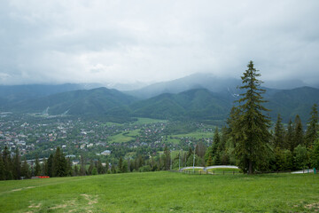 Fototapeta na wymiar Mountain panorama. Mountain peaks in cloudy weather. Foggy mountain peaks and a city in the gorge between them. Tatras hanging over the city of Zakopane.