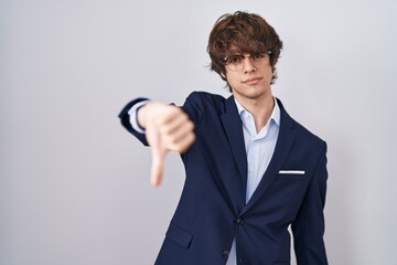 Naklejka premium Hispanic business young man wearing glasses looking unhappy and angry showing rejection and negative with thumbs down gesture. bad expression.