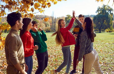 Happy friends meeting in an autumn park. Group of young men and women having fun on a sunny autumn...