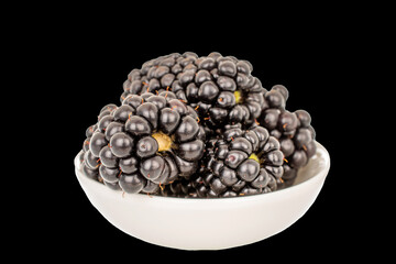 Several berries of organic blackberry with white ceramic plate, macro, isolated on black background.