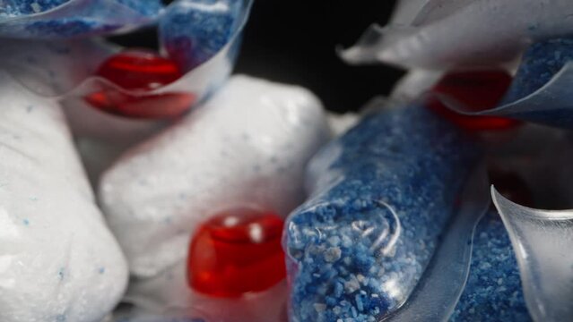 A multitude of soluble packets for dishwasher, capsules with red gel and white-blue powder. Dolly slider extreme close-up.