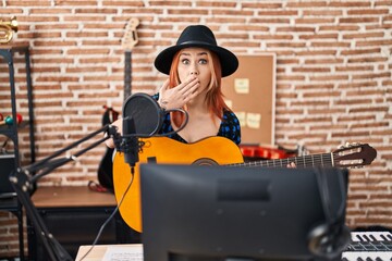Fototapeta na wymiar Young caucasian woman playing classic guitar at music studio covering mouth with hand, shocked and afraid for mistake. surprised expression