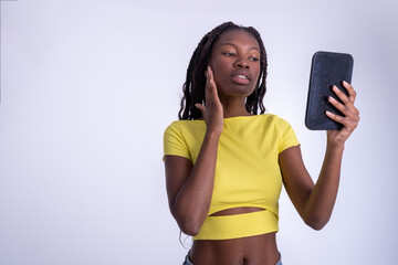 Mujer hermosa joven de color  que se pone las cremas delante de un pequeño espejo con un fondo...