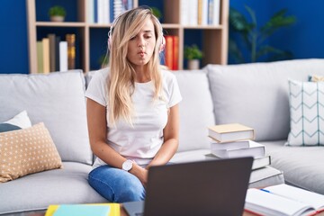 Obraz premium Young blonde woman studying using computer laptop at home making fish face with lips, crazy and comical gesture. funny expression.