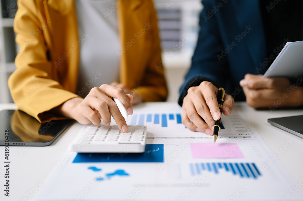 Poster business documents on office table with smart phone and laptop and two colleagues discussing data in