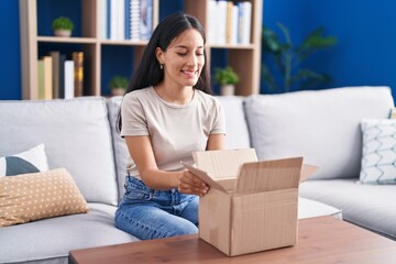 Young hispanic woman opening cardboard box smiling with a happy and cool smile on face. showing...