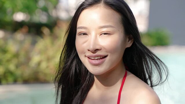Young Asian woman with black hair in bikini smiling by pool