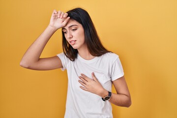 Obraz premium Young beautiful woman standing over yellow background touching forehead for illness and fever, flu and cold, virus sick