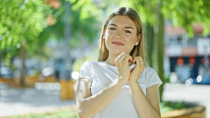 Fototapeta premium Young blonde woman smiling confident doing heart gesture with hands at park