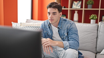 Young hispanic man watching tv sitting on sofa with relaxed expression at home