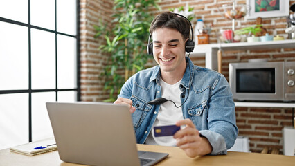 Fototapeta premium Young hispanic man having video call holding credit card at dinning room