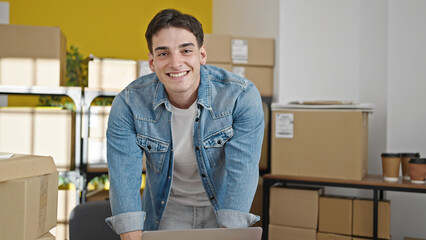 Young hispanic man ecommerce business worker using laptop standing at office