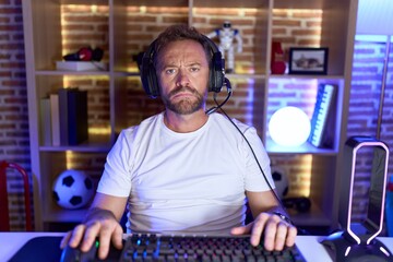 Middle age man with beard playing video games wearing headphones depressed and worry for distress, crying angry and afraid. sad expression.