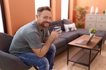 Middle age man drinking coffee sitting on sofa at home