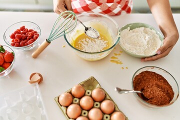 Young beautiful hispanic woman pouring flour on bowl with egg at the kitchen