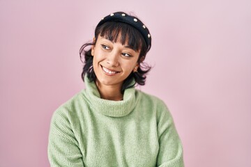 Young beautiful woman standing over pink background looking away to side with smile on face, natural expression. laughing confident.