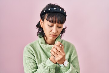 Young beautiful woman standing over pink background suffering pain on hands and fingers, arthritis inflammation