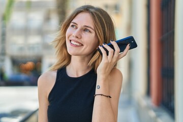 Young blonde woman listening to voice message at street
