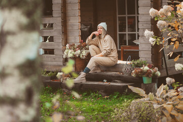 woman gardener relaxing in cozy autumn day, sitting on wooden stairs at house entryway. Enjoying warm october in the countryside, spending weekend outdoor