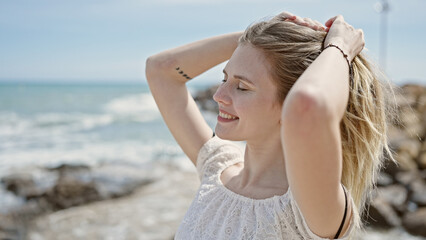 Young blonde woman tourist smiling confident touching hair at beach