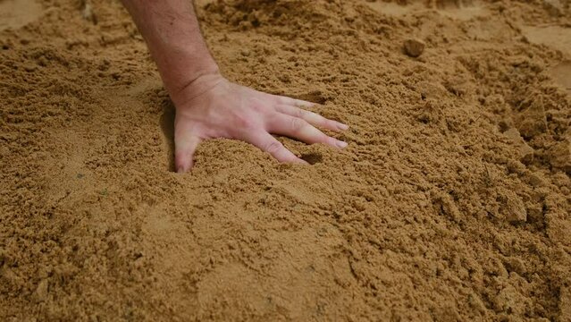 Slow motion while hand stamping pile of sand with bare hand making handprints.