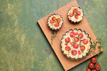 Unsweetened shortbread tartlets with feta cheese, cherry tomatoes and herbs on a wooden board on a green concrete background. Unsweetened pastries