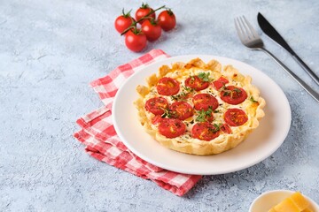 Unsweetened shortbread tartlets with feta cheese, cherry tomatoes and herbs on a white plate on a light concrete background. Unsweetened pastries,