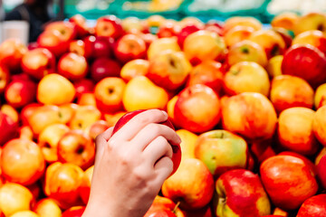 Woman's hand choosing apple on fruits shelf in supermarket