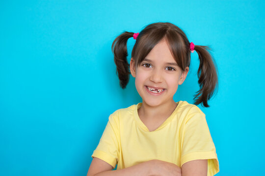 Close-up portrait of funny laughing cute toddler girl with missing baby tooth smile over blue