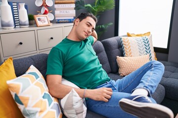 Obraz premium Young hispanic man relaxed with hand on head sitting on sofa at home