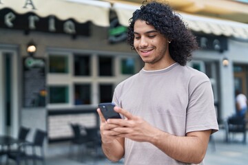 Fototapeta na wymiar Young latin man smiling confident using smartphone at coffee shop terrace