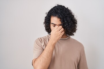 Hispanic man with curly hair standing over white background tired rubbing nose and eyes feeling...
