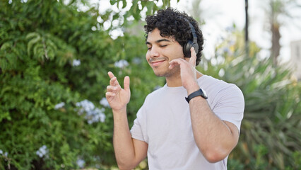 Fototapeta premium Young latin man listening to music and dancing at park