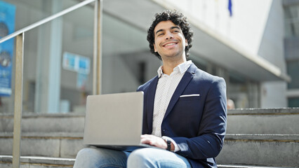 Fototapeta premium Young latin man business worker using laptop sitting on floor at street