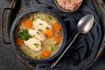 Fresh homemade chicken soup with noodles and vegetables on dark background. Supa de pui cu taitei.