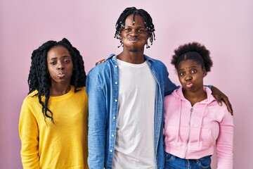 Group of three young black people standing together over pink background puffing cheeks with funny...