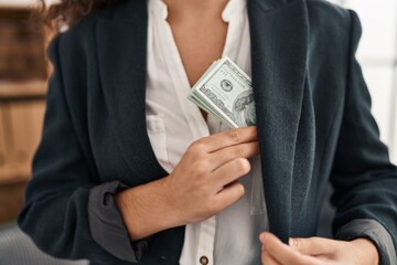 Young beautiful hispanic woman business worker save dollars on jacket over isolated black background