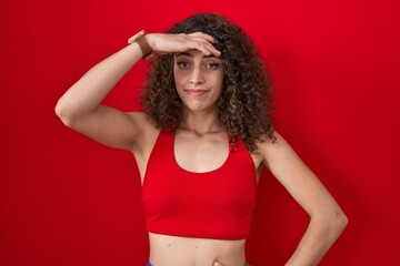 Hispanic woman with curly hair standing over red background worried and stressed about a problem with hand on forehead, nervous and anxious for crisis