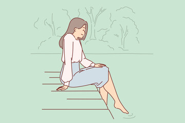 Woman is sitting on pier, lowering into water and enjoying silence and good summer weather