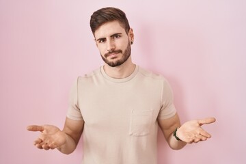 Hispanic man with beard standing over pink background clueless and confused with open arms, no idea...