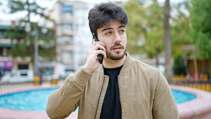 Young hispanic man talking on smartphone with serious expression at park