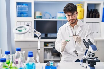 Young hispanic man scientist holding pills with tweezer at laboratory