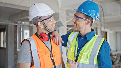 Two men builders smiling confident standing together at construction site
