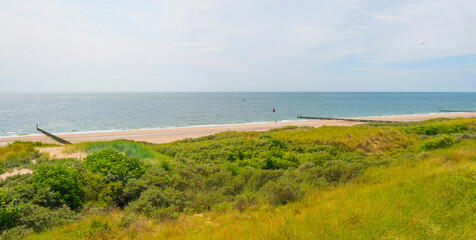 Sand beach along a sea under a dark blue cloudy sky in bright sunlight in summer, Zeeland, the Netherlands, June, 2023