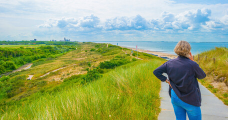 Sand beach along a sea under a dark blue cloudy sky in bright sunlight in summer, Zeeland, the Netherlands, June, 2023