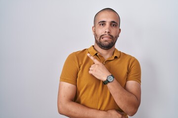 Hispanic man with beard standing over white background pointing aside worried and nervous with forefinger, concerned and surprised expression